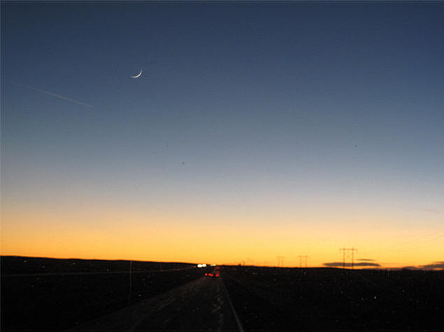 The  sliver of a new moon hovers above the setting sun.