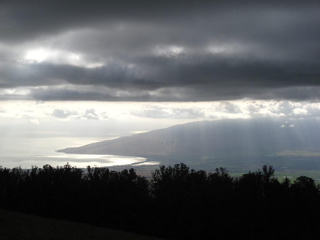 The sun shines through clouds onto the West Maui mountains.