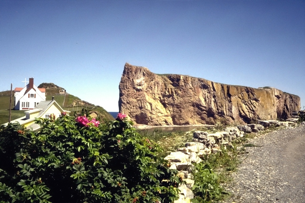 Percé Rock, juxtaposed with a house and a parking lot.